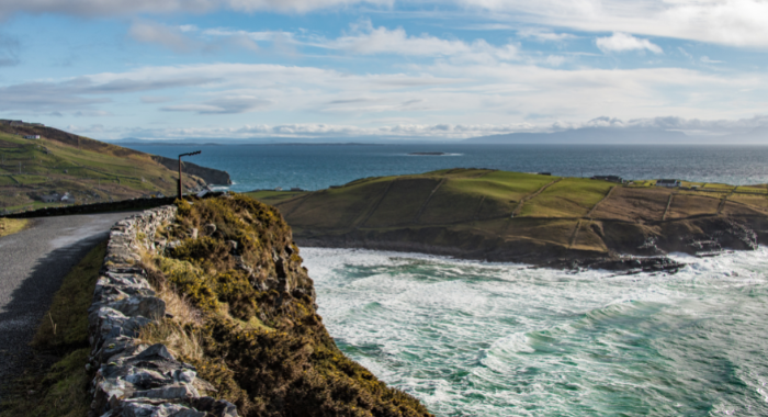 The Wild Atlantic Way in Ireland. There is a road on top of a cliff looking over choppy blue water and islands.