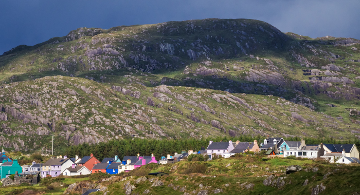 A row of multicoloured houses goes from left to right across the image, with a large hill in the background.