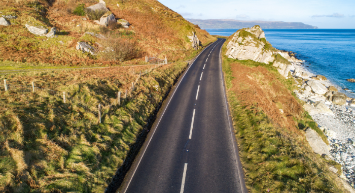 Causeway An arial view of the Causeway Coastal Highway. The road is central in the image with a grassy hill to the left and a cliff drop to the sea on the right.