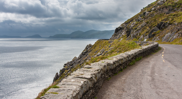 Dingle Peninsula A road with a brick wall to the left covering a drop to the sea, snakes to the left round a hilly range.