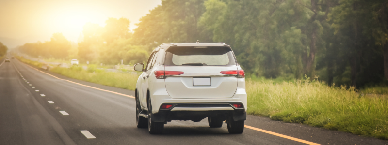 A white SUV driving along a road with greenery to the right of it.