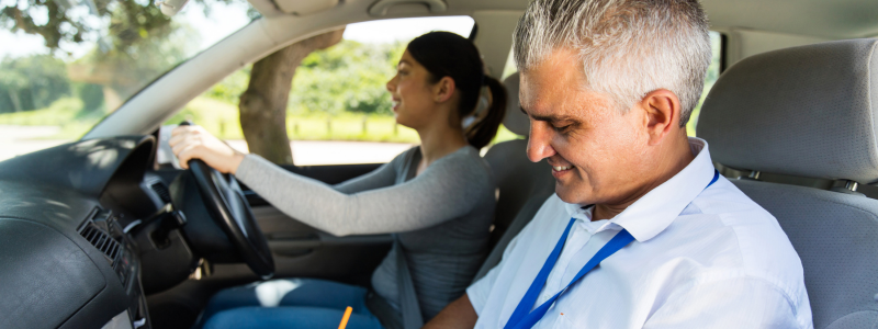 A person taking a driving test in a car with the instructor sat next to them.