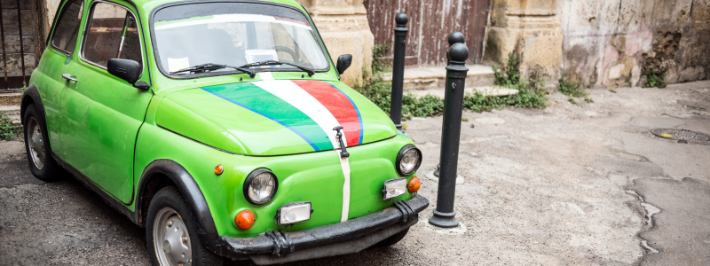 A green car with an Italian flag on the bonnet, parked up.