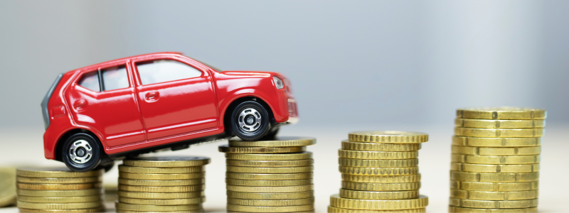 A red toy car on top of stacks of coins going from small to large from left to right, symbolising rising car prices.