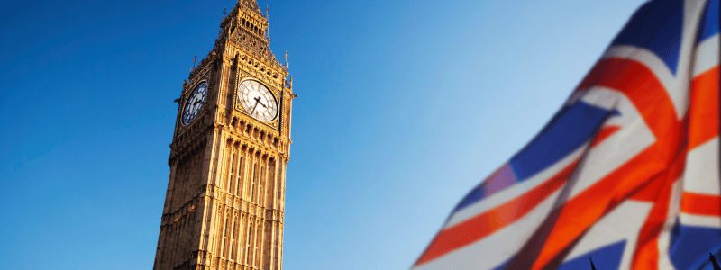 UK Big Ben Big Ben against a light blue sky, with a UK flag waving at the right of the image.