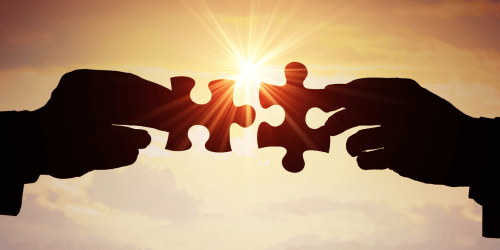 Two hands push jigsaw pieces together, with sun shining through the gaps.