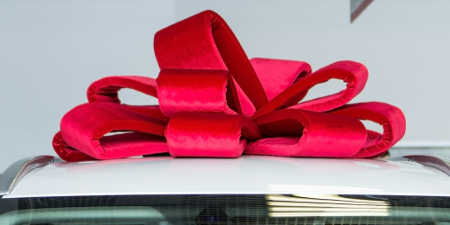 A close up of the top of a car, with a large red bow on, indicating that the car is new or a present.