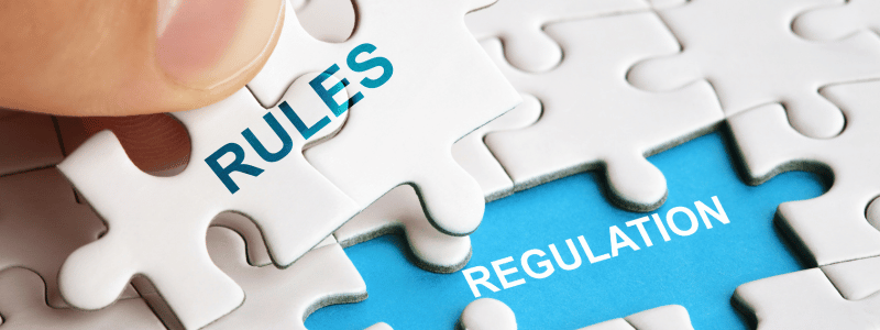 Rules Regulation Jigsaw Pieces Someone places a jigsaw piece into a gap. 'RULES' is written on the jigsaw and 'REGULATION' in the gap, representing the relationship between the two.