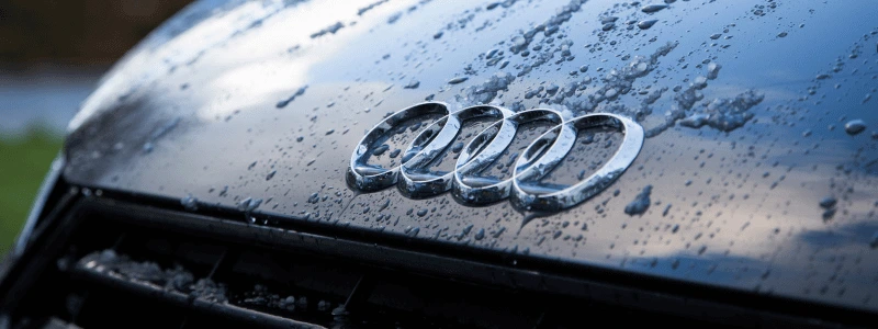 Audi A1 Logo Close Up (1) The Audi logo close up on a black car, with water droplets around it.