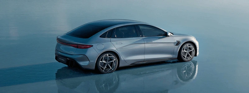 A light blue BYD Seal driving through shallow water, likely on a beach.