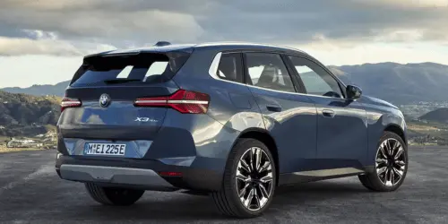 A BMW X3 Plug-in Hybrid parked in front of a mountain range on a cloudy day.