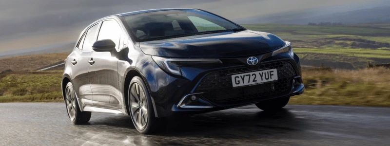 A black Toyota Corolla Hatchback driving in a countryside setting.