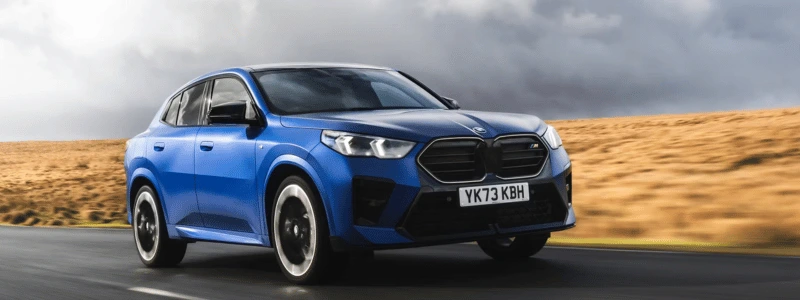 A blue 2025 BMW X2 driving on a country road. 