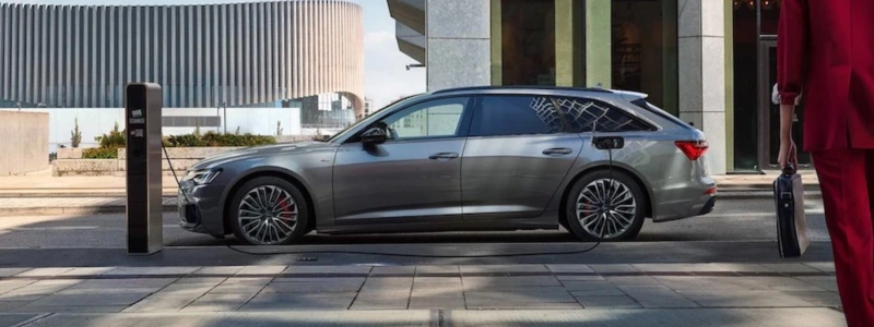A grey Audi A6 Plug-in-Hybrid estate car charging in a city setting.