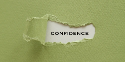 The word confidence on a piece of paper, appearing out of a cut out on a green piece of paper.
