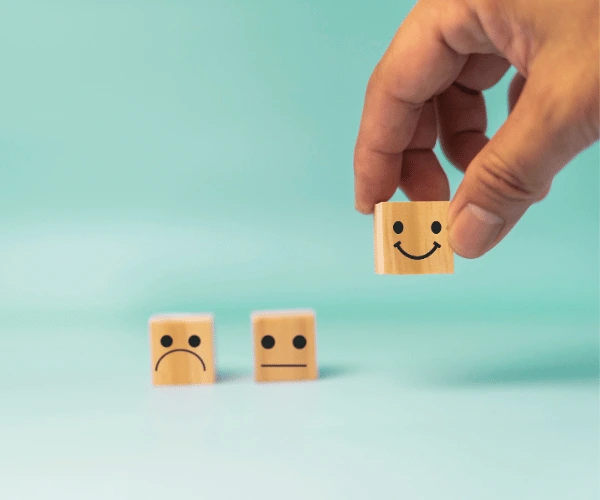 A hand placing a block with a smile drawn on next to similar blocks with sadder expressions.