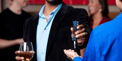 A person handing keys over whilst holding a glass of wine, signalling that the other person is a designated driver.