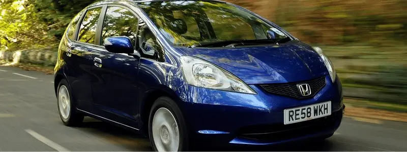 A blue Honda Jazz driving on a rural road.