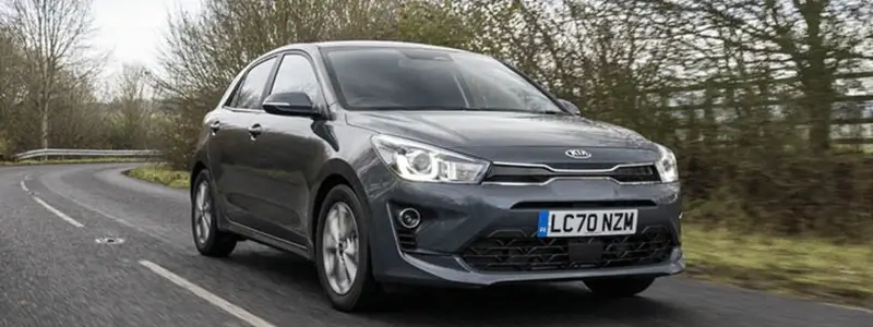 A black Kia Rio on a rural road.
