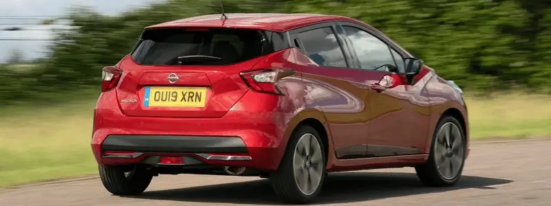 A red Nissan Micra on a rural road.