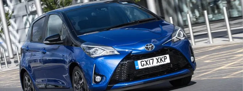 A blue Toyota Yaris driving on a road.