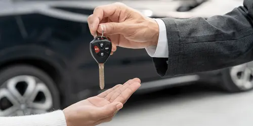 A handover of car keys between two people, with a car in the background.