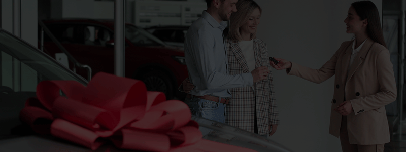 A close up of the top of a car, with a large red bow on, indicating that the car is new or a present.